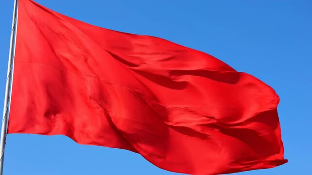 Vibrant red flag waving in clear blue sky.