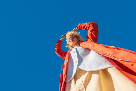 Low angle view of dancing woman with smartphone in orange coat