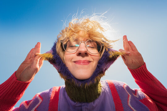 Woman adjusting colorful knit hood with eyes closed outdoors
