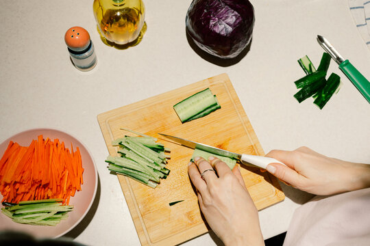 Young woman chopping cucumber salad for dinner.