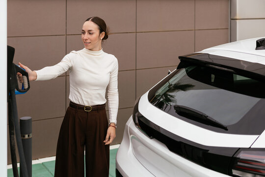 Young woman charging electric vehicle at station