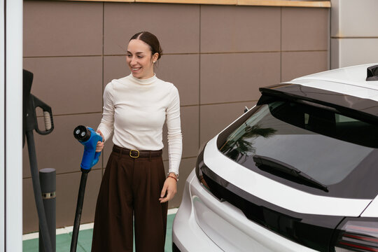 Young woman charging electric vehicle at station