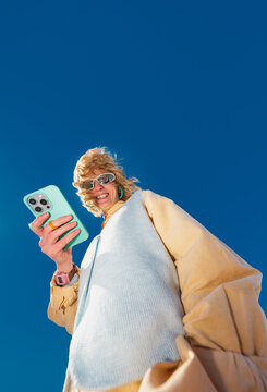 Low angle portrait of smiling woman holding smartphone outdoors