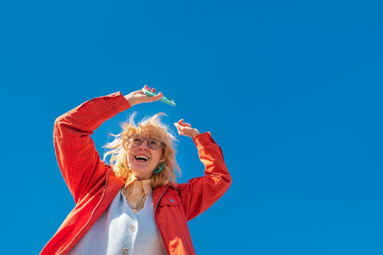 Low angle portrait of joyful woman dancing with smartphone