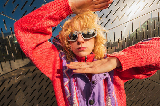 Woman in sunglasses posing with hands against metal wall