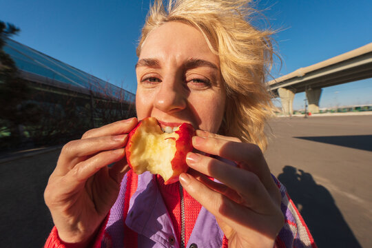 Woman eating red apple in sunny urban environment