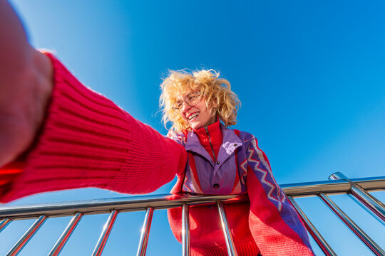 Smiling woman leaning over railing reaching toward camera
