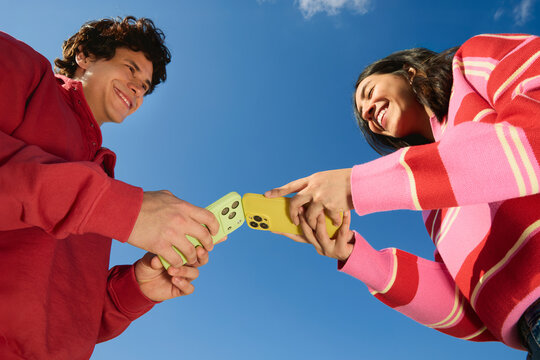 Man and woman airdropping with smartphones outdoors smiling