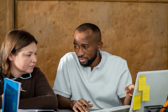 Two employees working in office together at desk with laptop