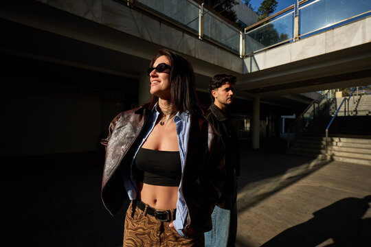 Two people stand in sunlight near a building in the city