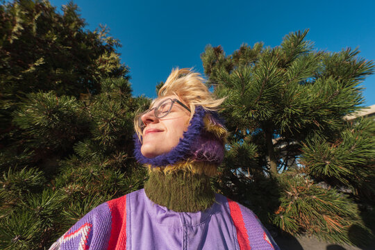 Woman in knitted hood enjoying sunlight among pine trees
