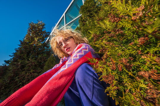 Woman in colorful sweater sitting among greenery near glass building