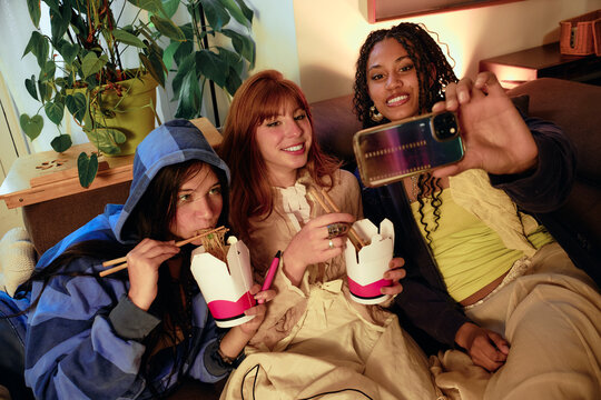 Friends eating takeout and taking selfie on couch
