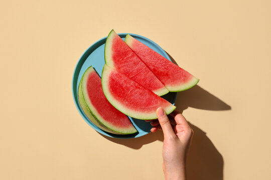 Watermelon slices on a blue plate with a hand reaching for a piece