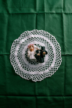 a broken bride and groom figurine resting on a crocheted doily