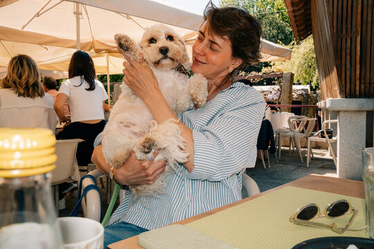 Woman Holds Dog While Sitting at Outdoor Cafe on a Sunny Day