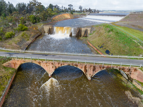 Arched road bridge crossing water rushing over a reservoir spillway