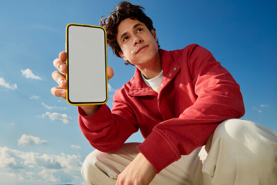 Man holding smartphone with blank screen outdoors under blue sky