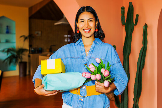 Smiling woman holding gifts and tulips at colorful home ugc