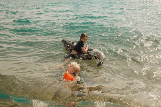 The children are swimming in the water with an inflatable crocodile