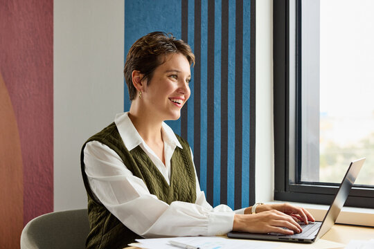Smiling businesswoman types on a laptop
