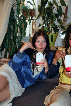 Woman eating noodles from takeout box on sofa
