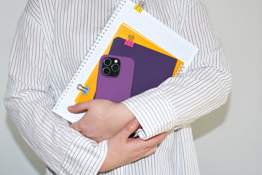 Student holds notebooks and phone close to chest