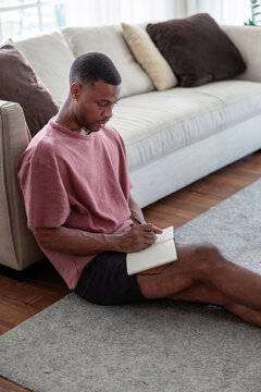 Man sitting on floor, writing in notebook.