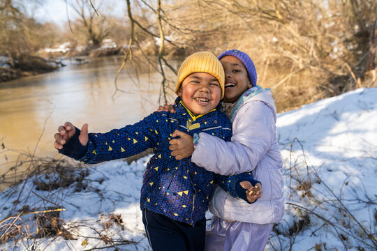Joyful children playing in snow by river in winter sunlight
