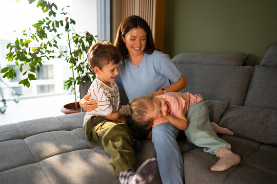 Mother laughing with children on sofa at home