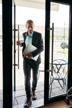 Professional Man Steps Into Bright Cafe With Laptop in Hand