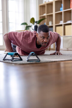 Man doing push-ups with handles nearby in a bright room.