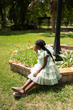 Girl Sitting in Garden Wearing White Ruffled Dress and Glasses