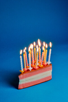 a slice of cake with many lit birthday candles on a blue background