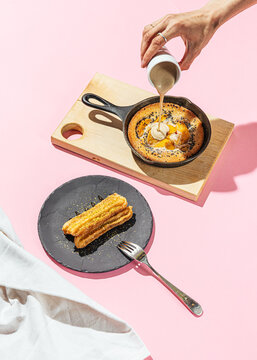Hand pouring sauce into peach pancake with a side of churros