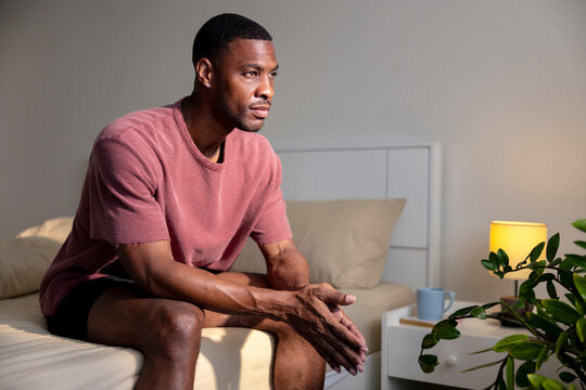 Man sits on bed, looking thoughtful in morning light.