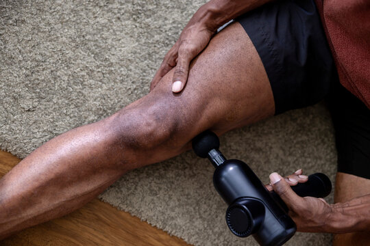 Man massages leg with massage gun on carpet.