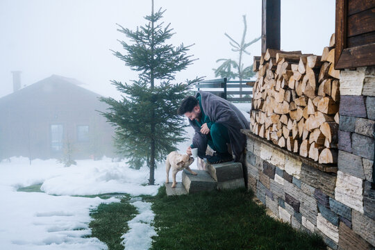 Man with coffee and French bulldog outside snowy mountain cabin
