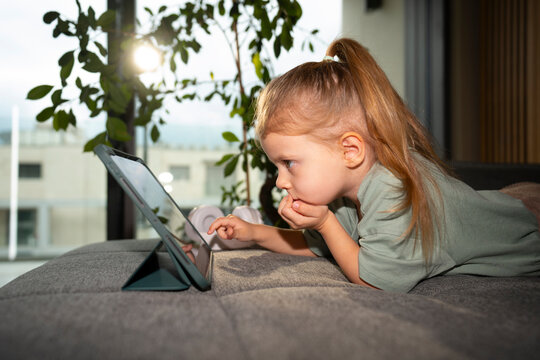Child playing on tablet while lying on couch