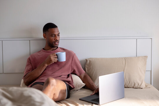 Man in bed with laptop and coffee mug.