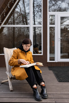 A woman draws in a sketchbook on the street near a house.