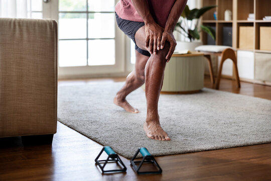 Man holding knee while stretching at home in living room