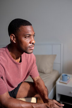 Pensive man sits on bed, looking towards the light.