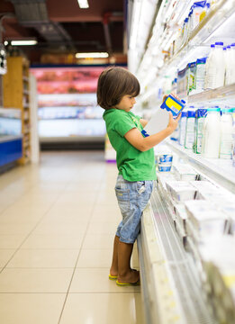 Child choosing milk carton in supermarket grocery aisle
