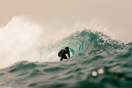 An elite surfer carve deep inside the hollow barrel of a massive wave