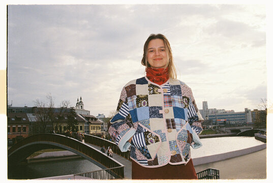 Smiling person wearing a patchwork jacket stands on a bridge in Minsk