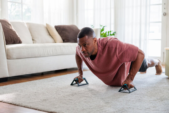 Man doing push-ups with handles in a bright living room.