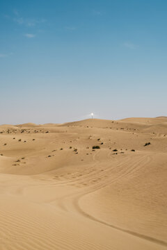 Sand dunes with tire tracks under midday sky