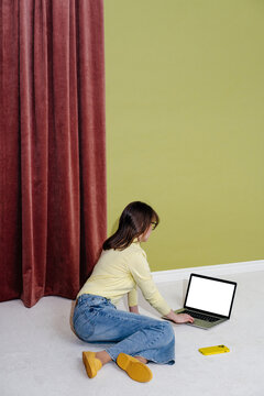 Person Sitting on Floor Using Laptop with Smartphone Nearby