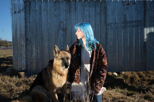 Woman stands with dog near metal fence in the sun